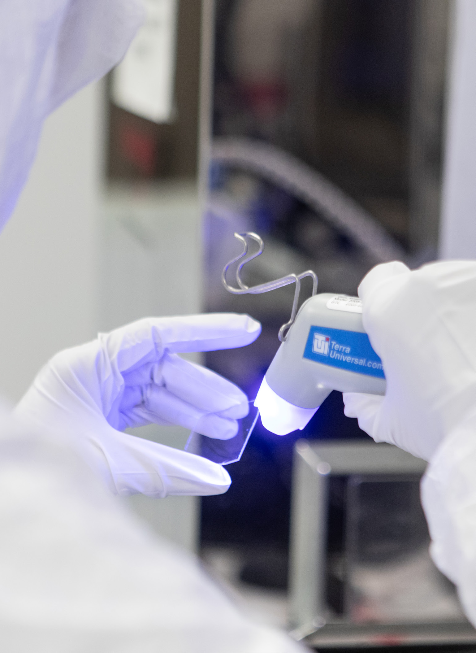 a pair of gloved hands holding a slide for a microscope and a dropper